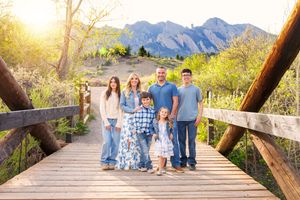 Family of six poses on a wooden bridge with Flatirons mountains and golden sunset in Boulder, Colorado.