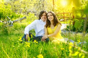 A couple sits together in a spring meadow surrounded by yellow wildflowers and grass.