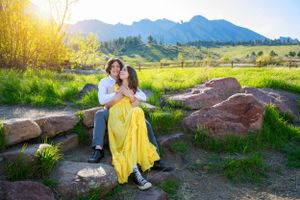 A couple poses on rocky terrain with mountain views in golden evening light.