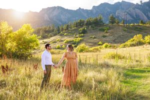 Couple walks hand in hand through golden mountain meadow at sunset in Boulder Colorado.