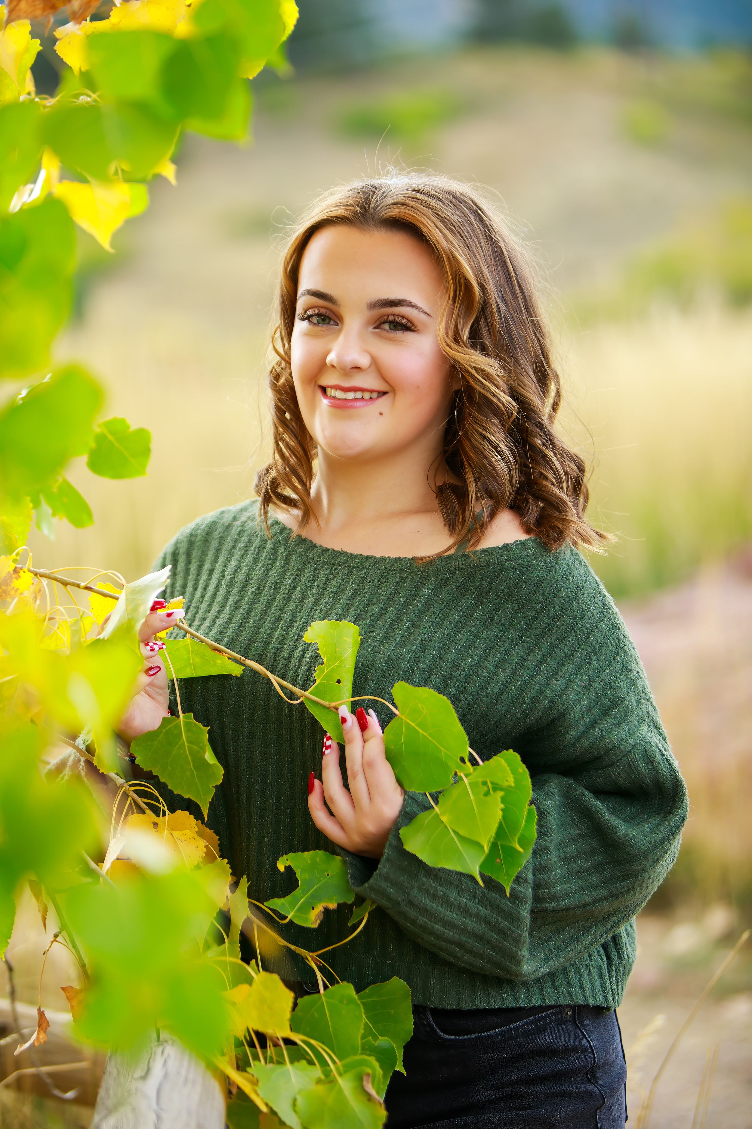 Person in green sweater poses among vibrant grape vines in a sunny vineyard setting.