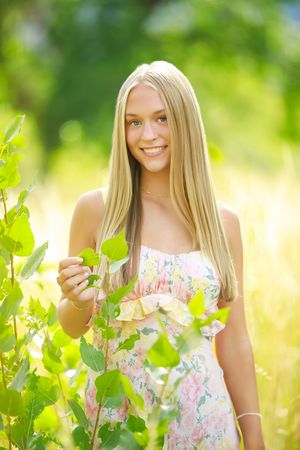 A floral sundress-clad figure poses in a sunny garden setting with green foliage and warm natural lighting.