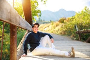 Person relaxing on wooden boardwalk with mountain view at sunset.