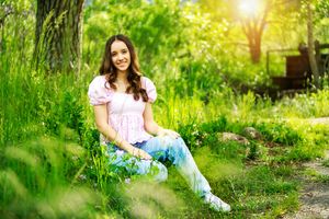 Someone in a pink top and blue jeans sits in lush green grass with sunlight filtering through trees.
