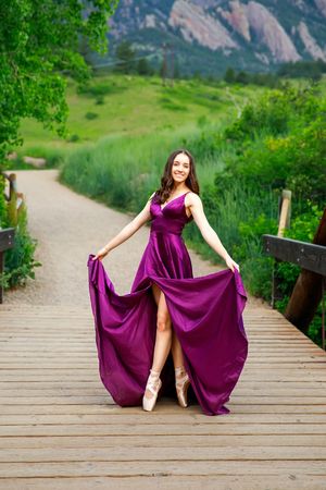 A flowing purple gown is showcased on a wooden boardwalk path with mountains and greenery in the background.