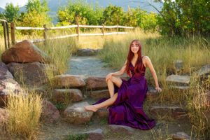 A model in a deep purple dress sits gracefully on natural rock formations at golden hour.