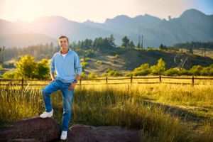 Person in blue sweater sitting on rock with mountain backdrop at sunset.