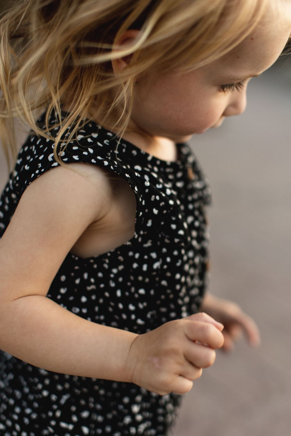 Close-up of a toddler girl in a black spotted dress with blonde hair looking down.