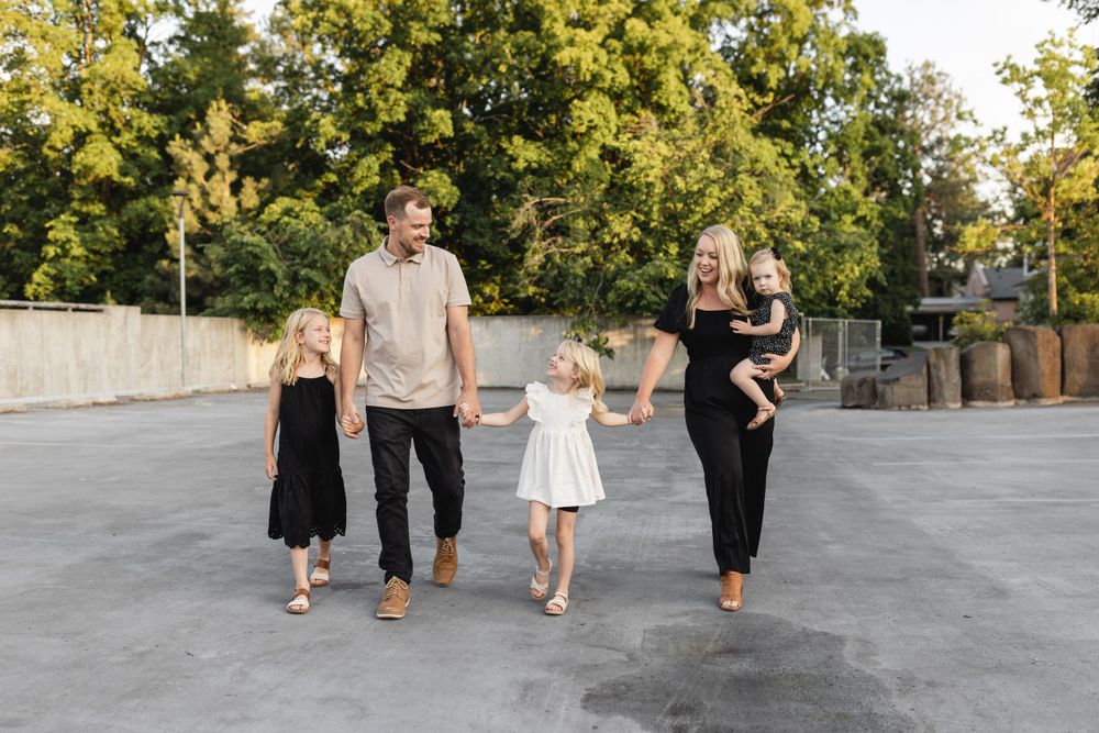 Joyful family of five holding hands and walking together outdoors near trees in warm sunlight.