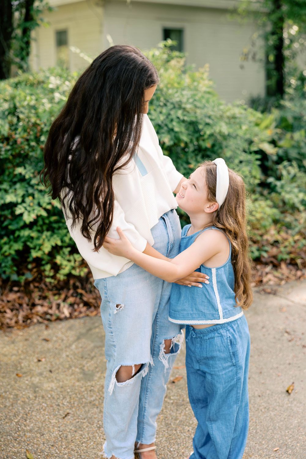A mother and young daughter in denim outfits share a tender embrace outdoors, smiling at each other.