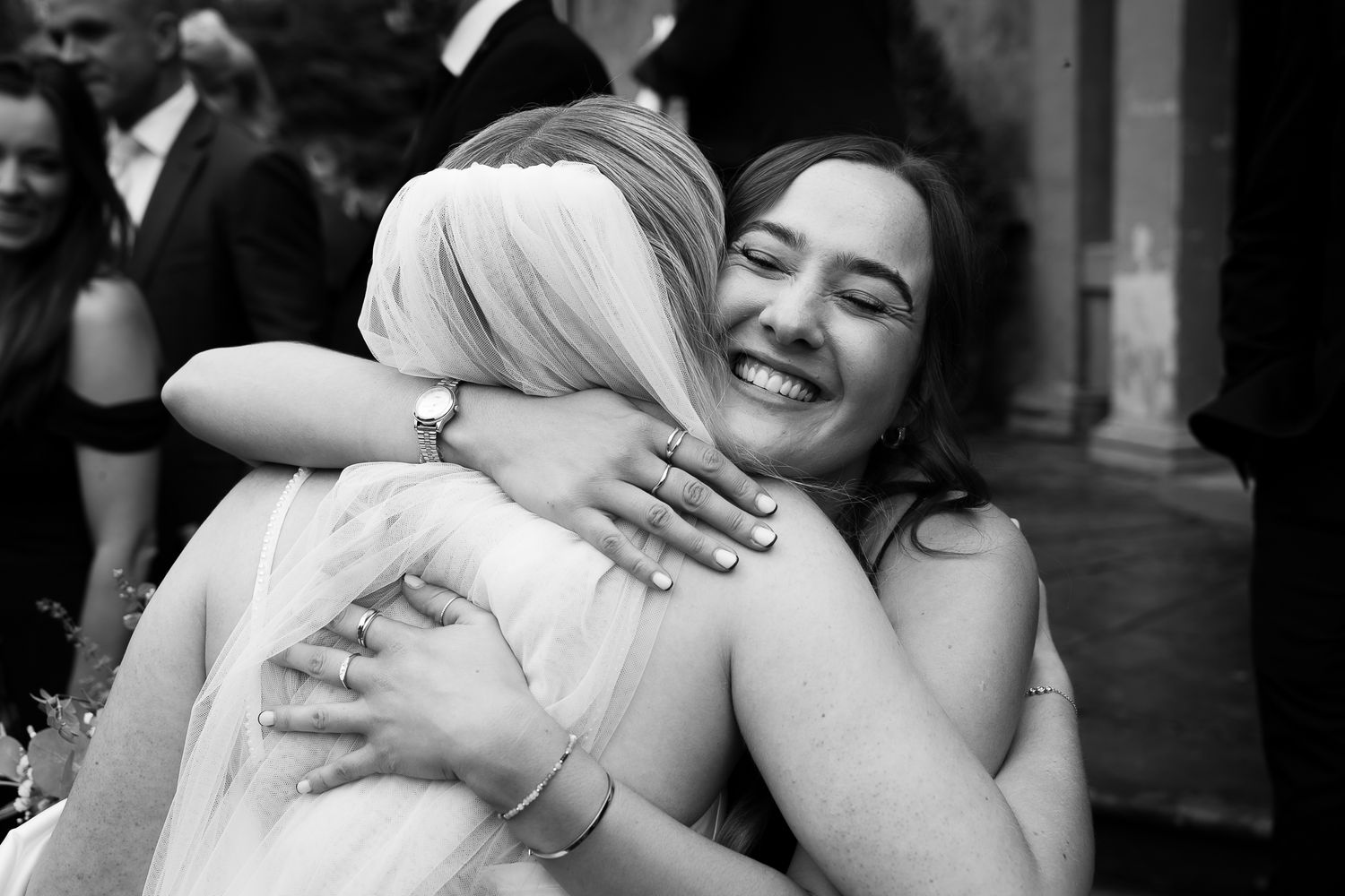 Black and white candid photo capturing a joyful embrace during wedding celebrations.