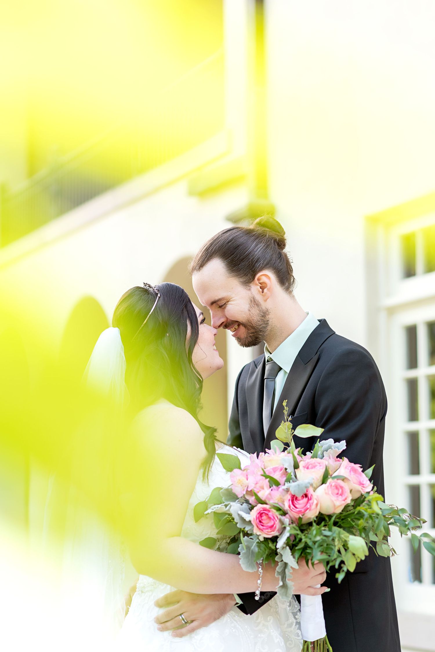 Wedding couple embracing with pink bouquet against bright yellow background at Elsie Perrin Williams Estate in London ontario.
