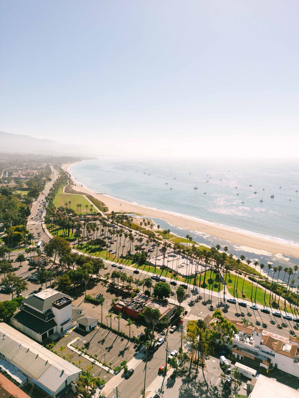 Aerial panoramic view of a coastal city with palm-lined streets and beachfront properties stretching along the ocean.