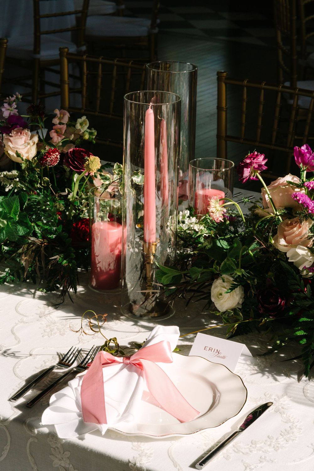 Elegant wedding table setting with pink candles, floral centerpiece, and a white napkin tied with a pink bow on a white plate.