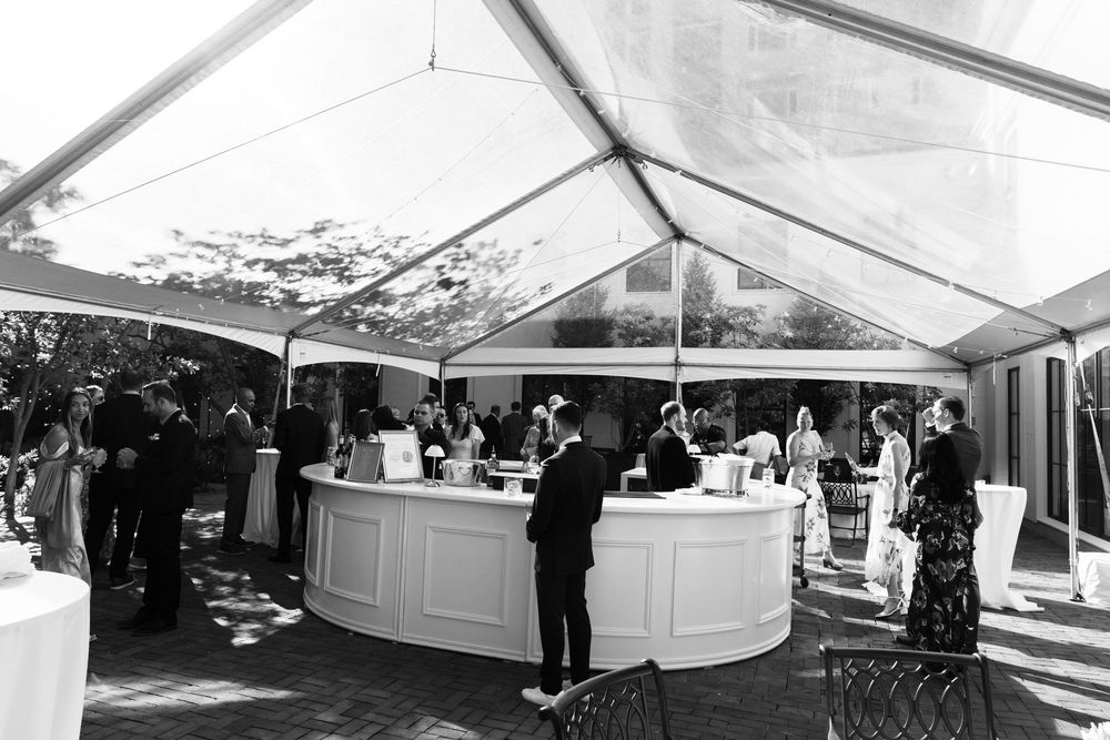 Black and white photo of elegant outdoor wedding reception under a clear tent with a white circular bar.