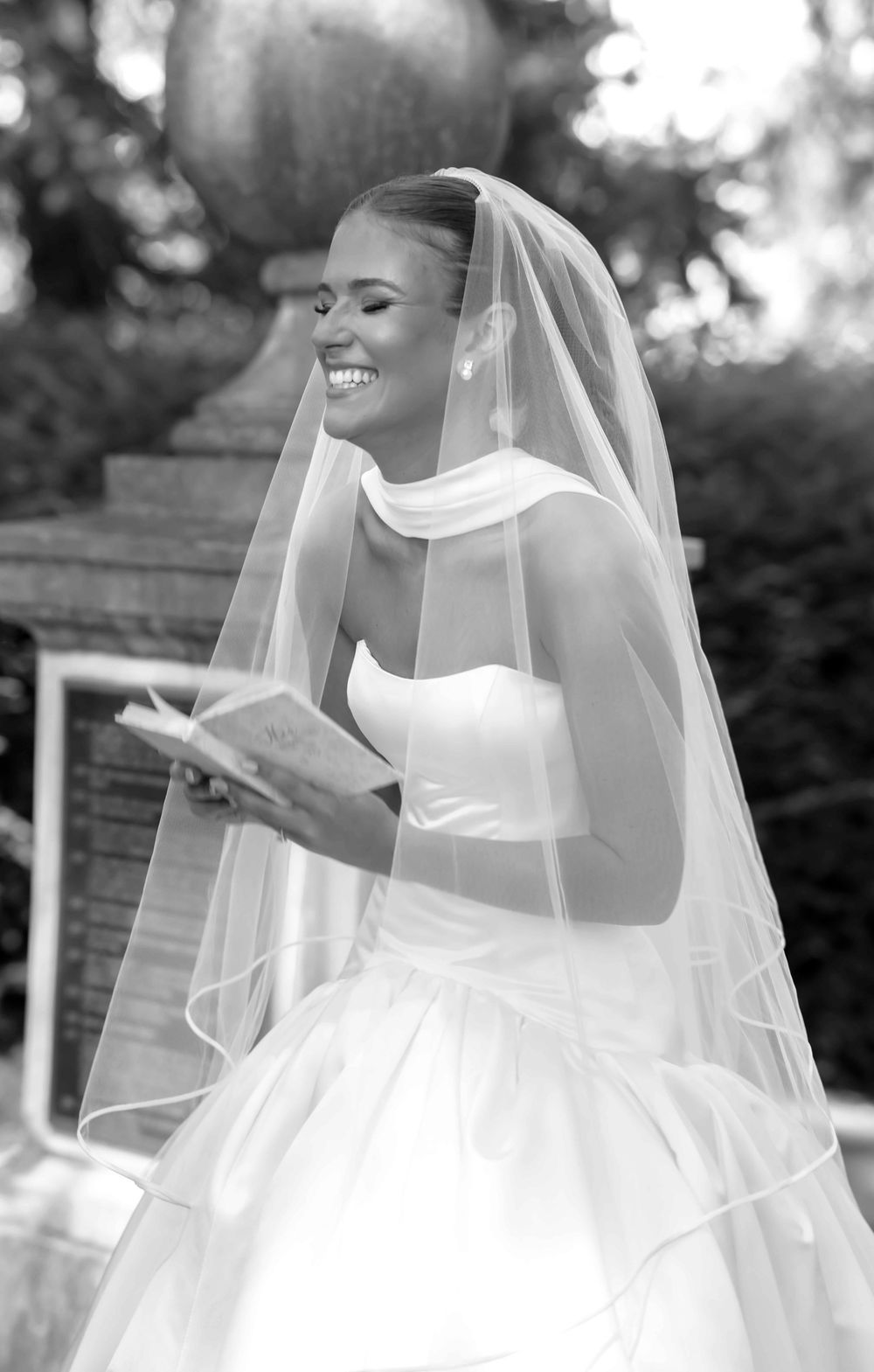 A beautiful bride in a white strapless wedding gown and flowing veil poses joyfully in a black and white photo series.