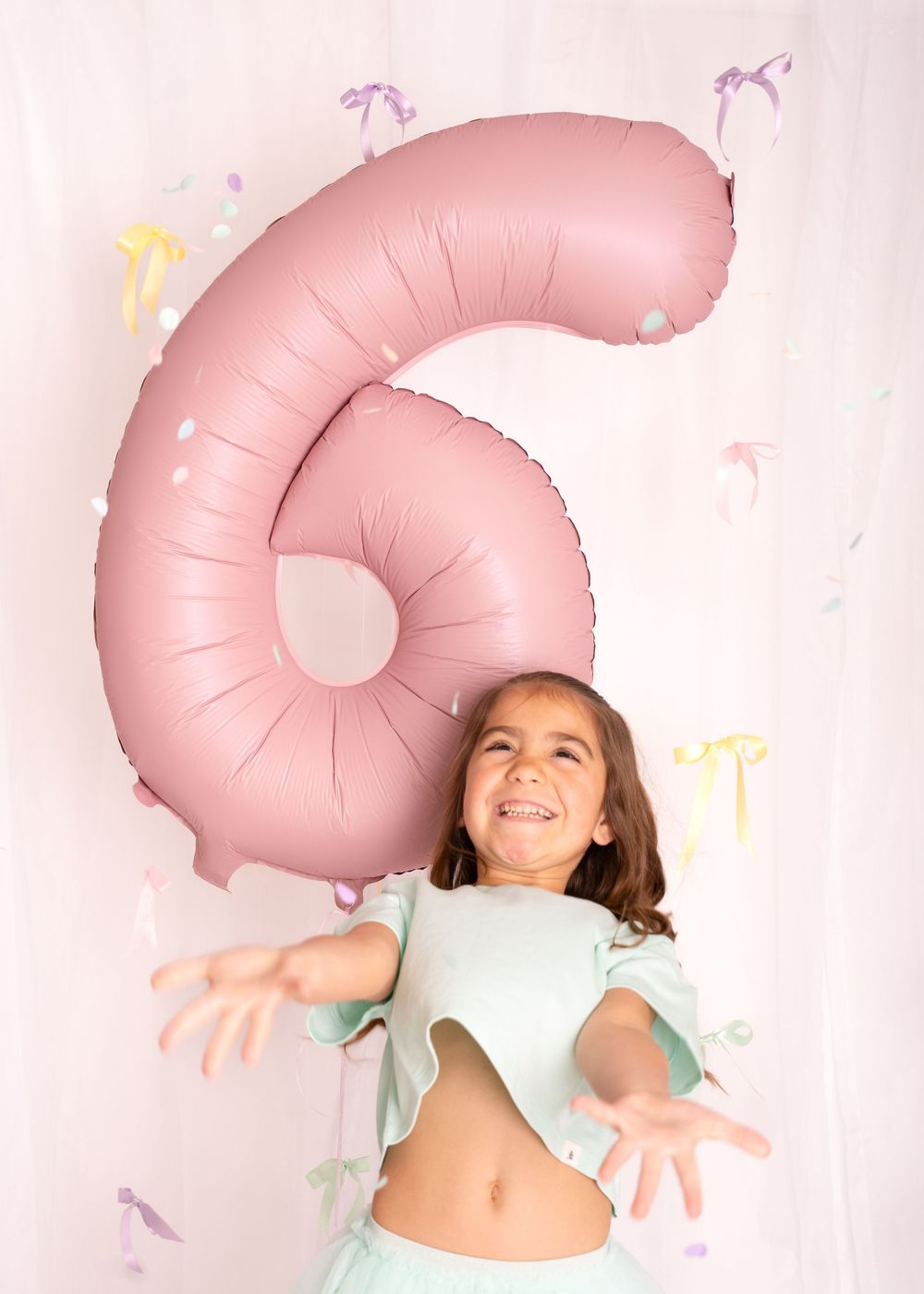 A young girl celebrates her 6th birthday, laughing joyfully in front of a large pink number 6 balloon.