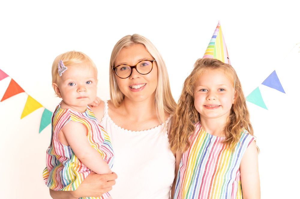 Colorful rainbow striped dresses against white background with festive triangle bunting flags overhead.