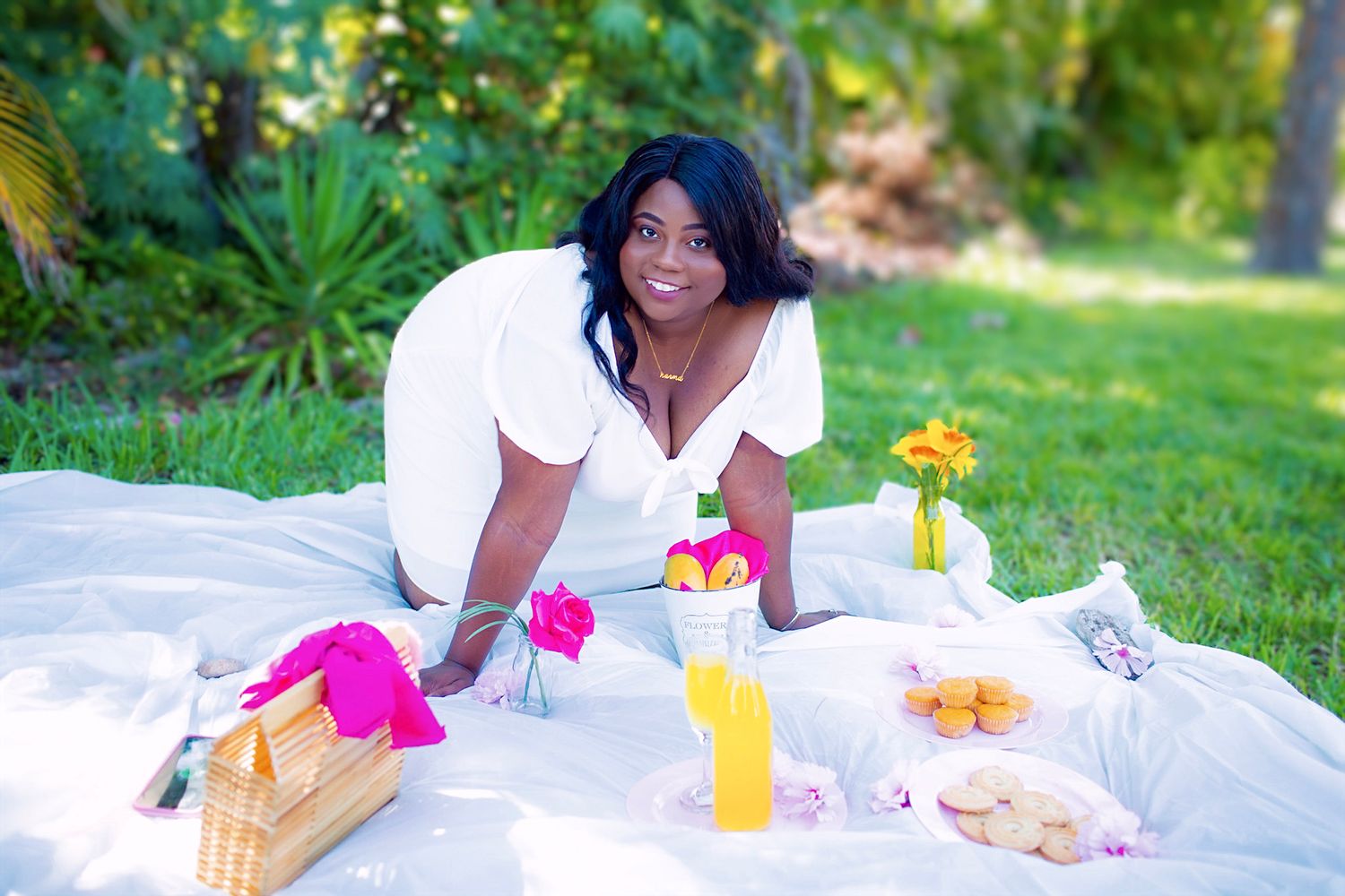 A picnic setup on white blanket with colorful drinks and snacks in sunny garden setting.