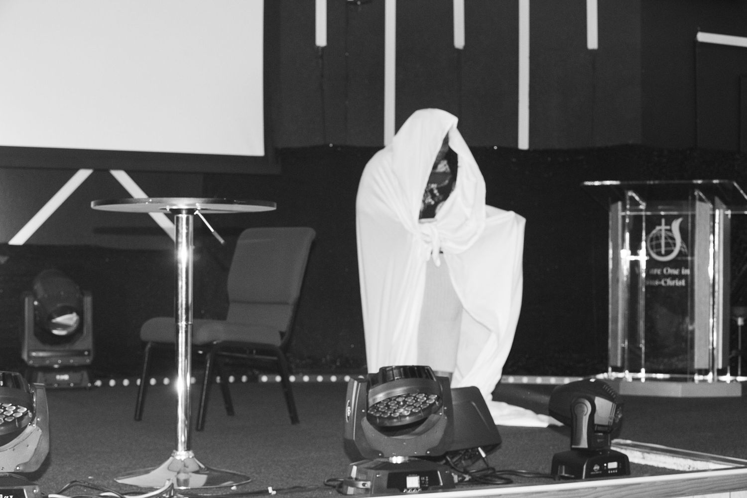 A ghostly white figure crouches on a dark stage with musical equipment visible in the background.