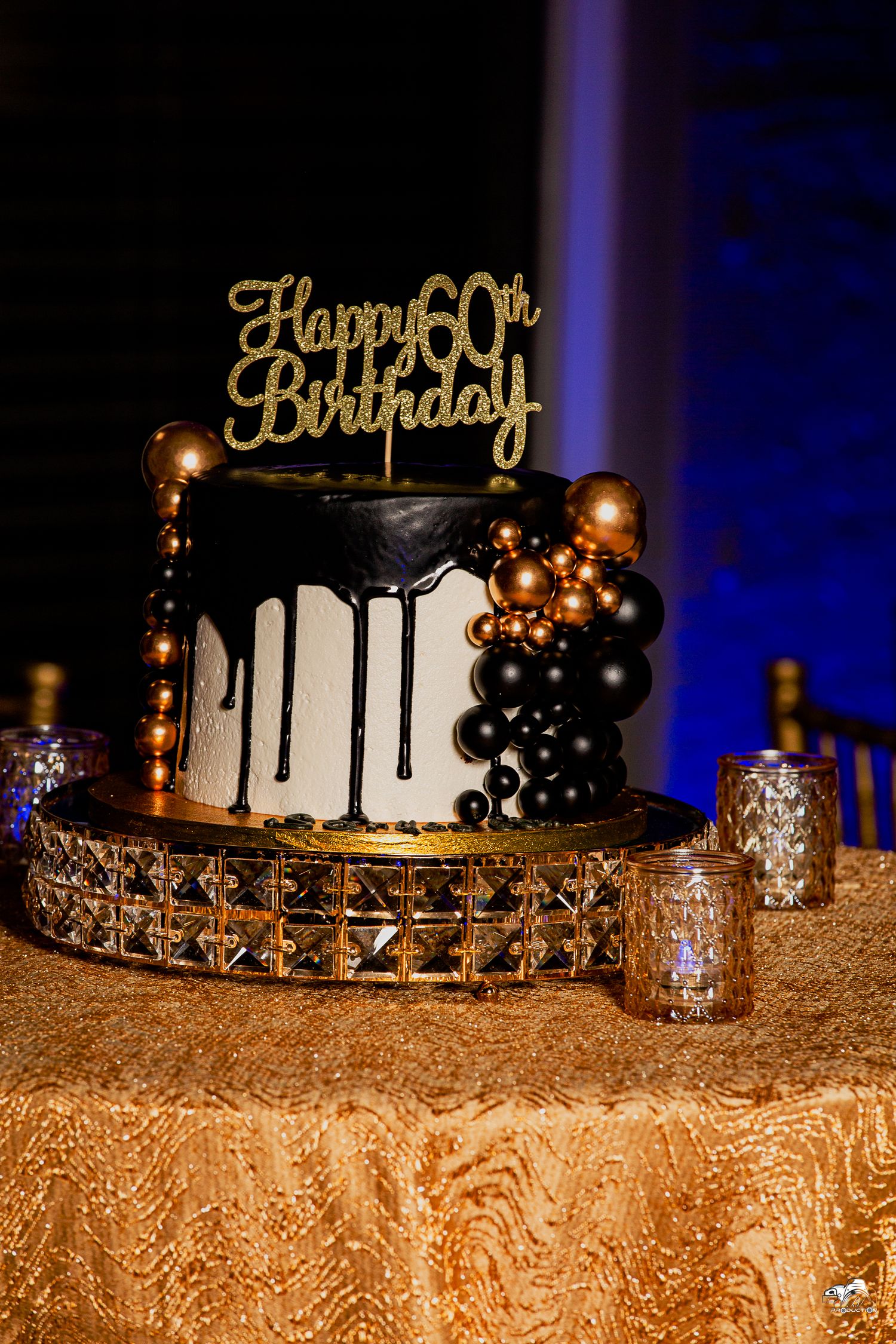 An elegant black and white 50th birthday cake with gold topper and balloon decorations.
