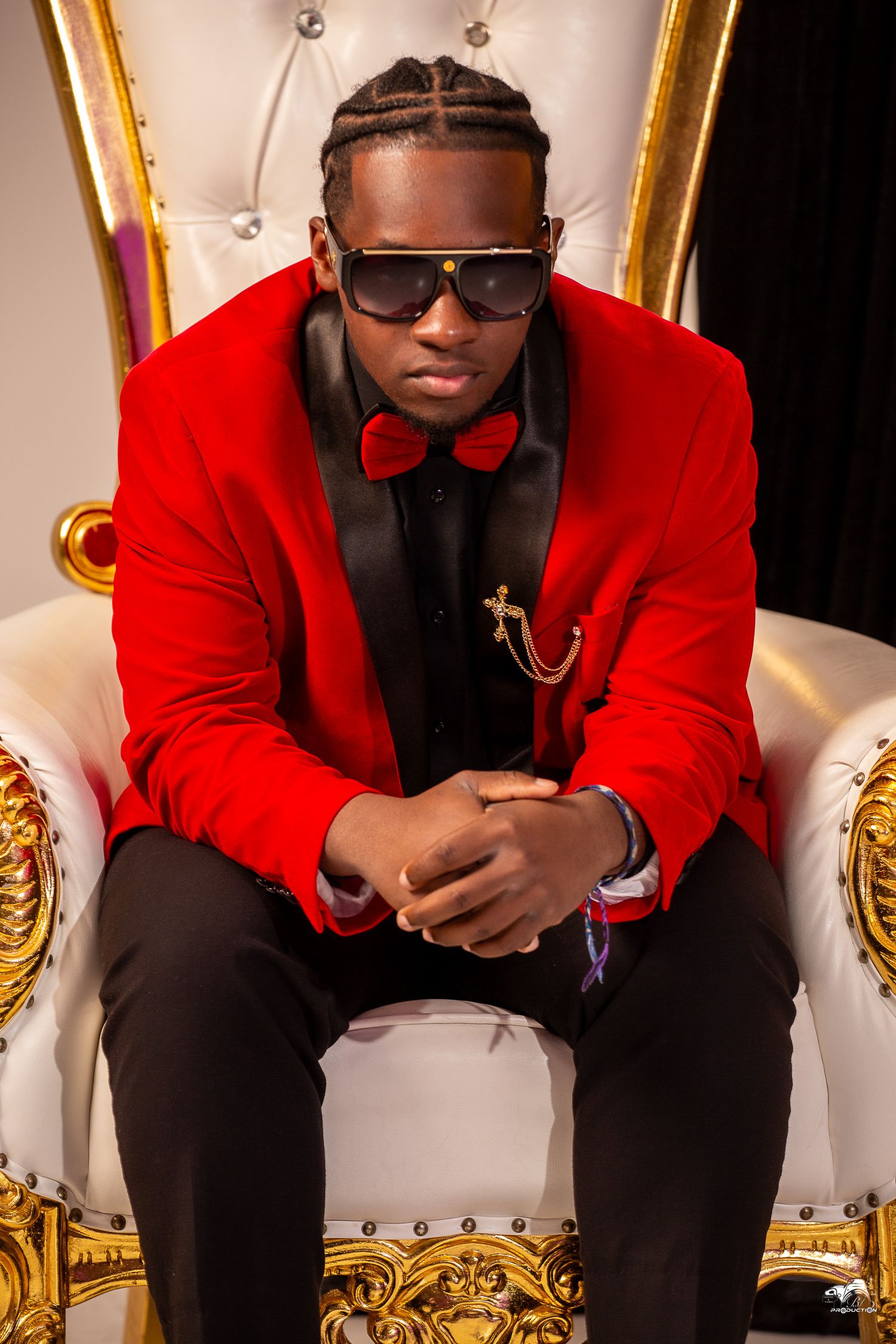 Stylish portrait of performer in red blazer and bow tie seated on ornate white throne.