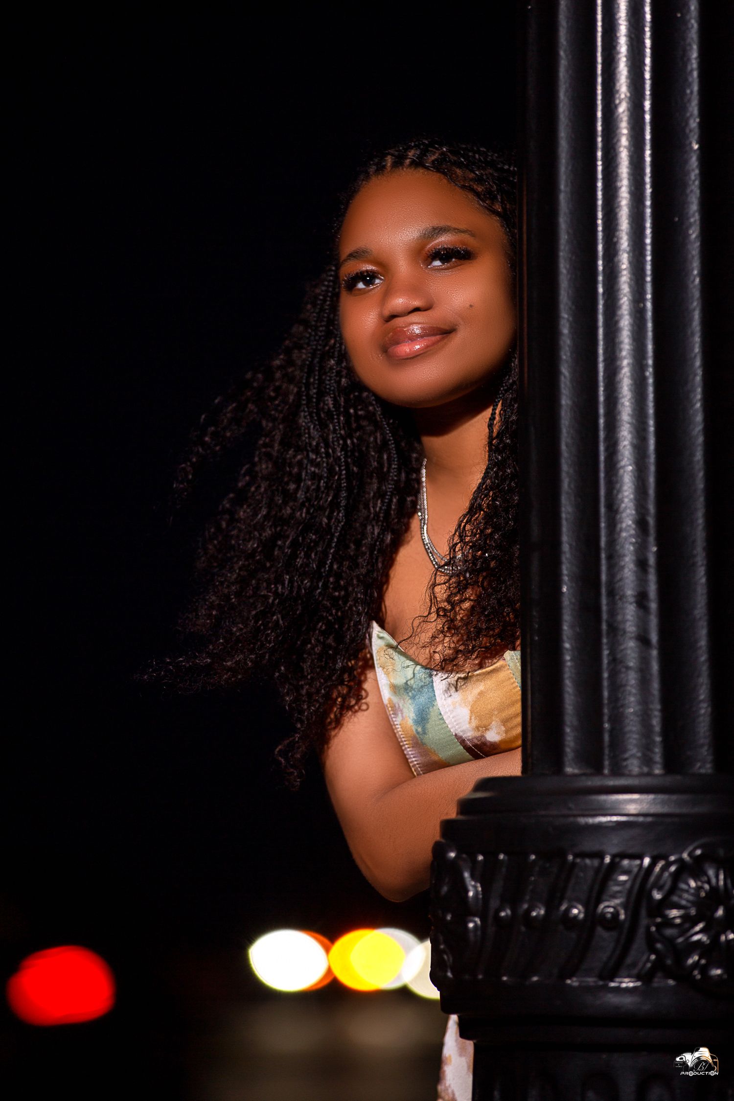 Portrait of woman with curly hair posing against ornate black pillar at night.