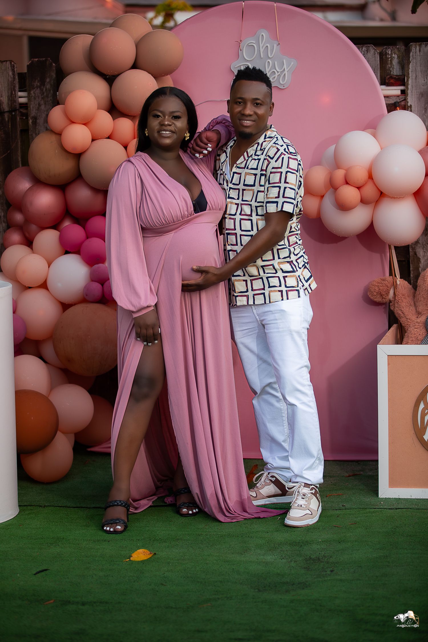 Couple posing at baby shower with pink arch and balloon decorations.