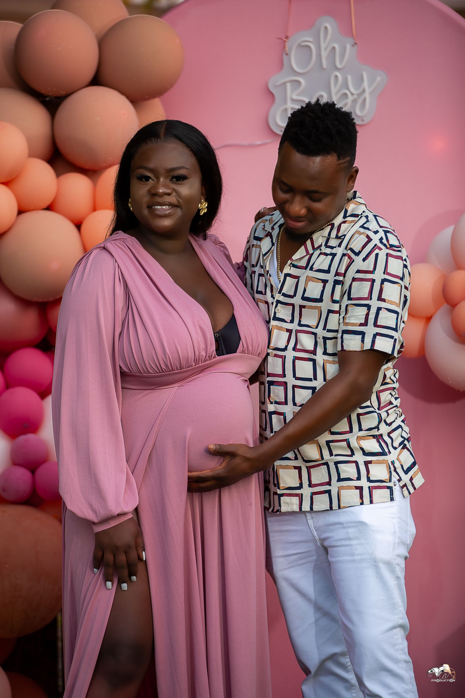 Expectant couple sharing intimate moment at baby shower with balloon backdrop.