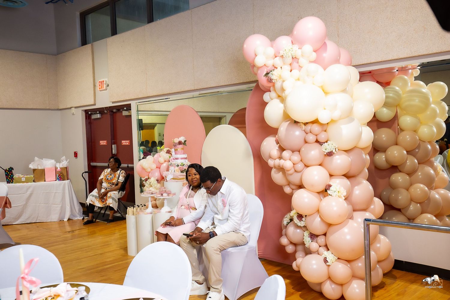 An indoor celebration setup with pink balloon arrangements and white tables.