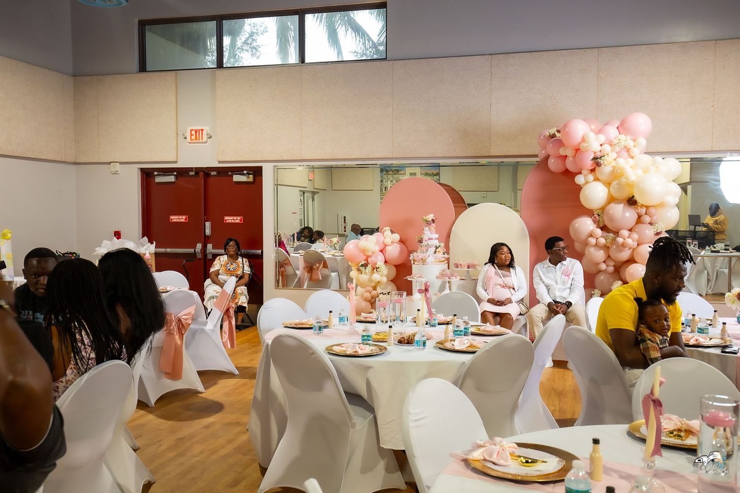 An elegant party venue with white chairs, tables and pink balloon decorations.