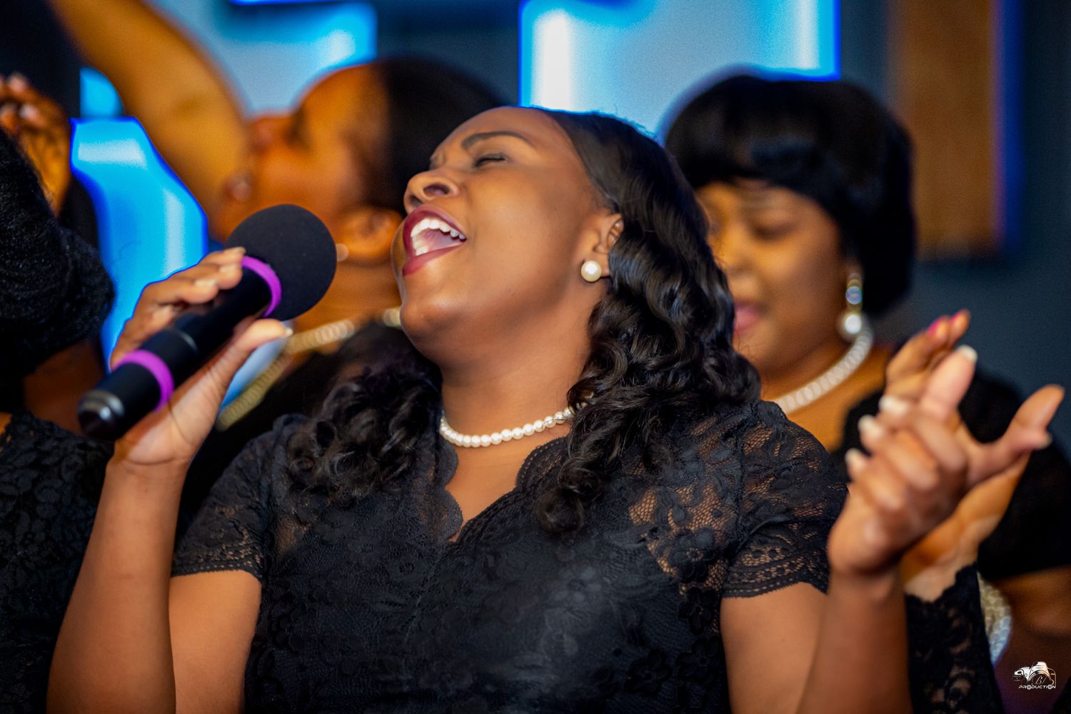 A passionate gospel performance featuring a singer in a black dress with pearl necklace.