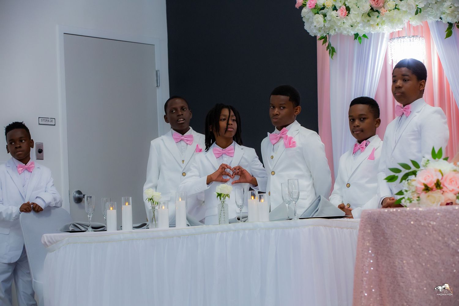 Wedding party in white suits and pink accessories stand behind reception table.