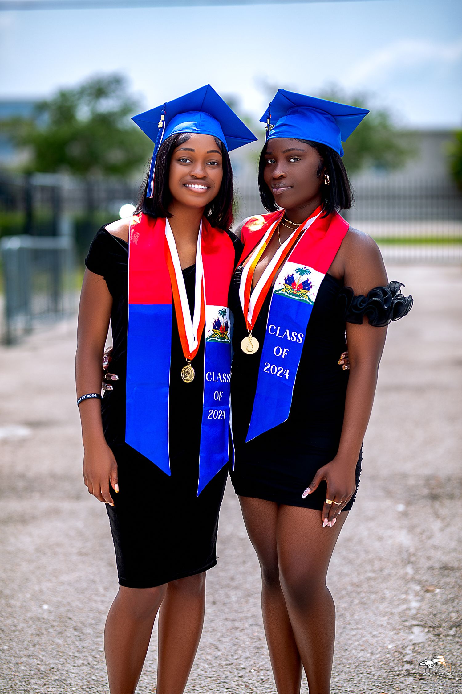 Two graduates in matching blue caps and Haitian stoles celebrate commencement together.