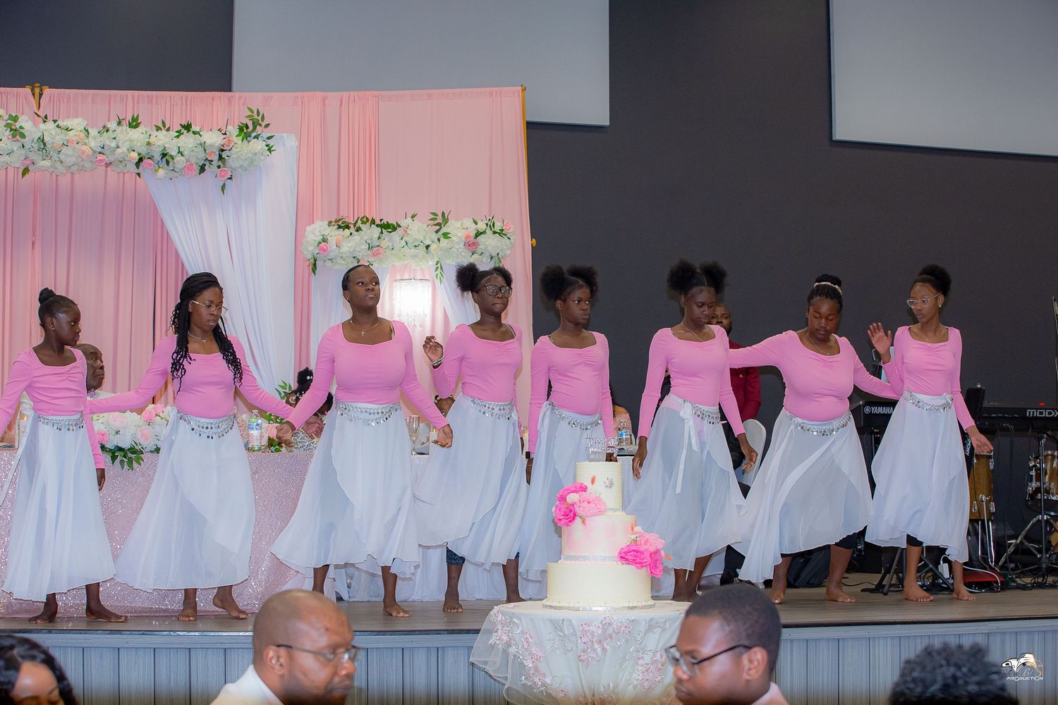 Wedding party members in pink and white outfits perform a choreographed dance.