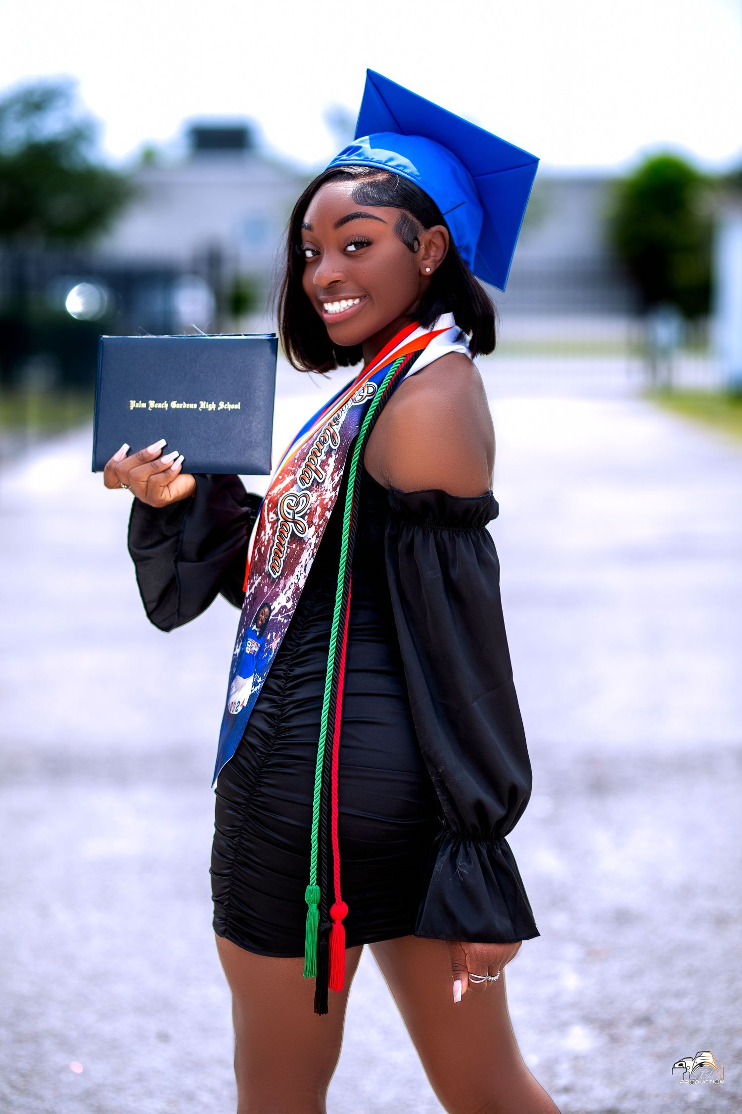 Graduate in blue cap and black dress holds diploma while celebrating academic achievement.