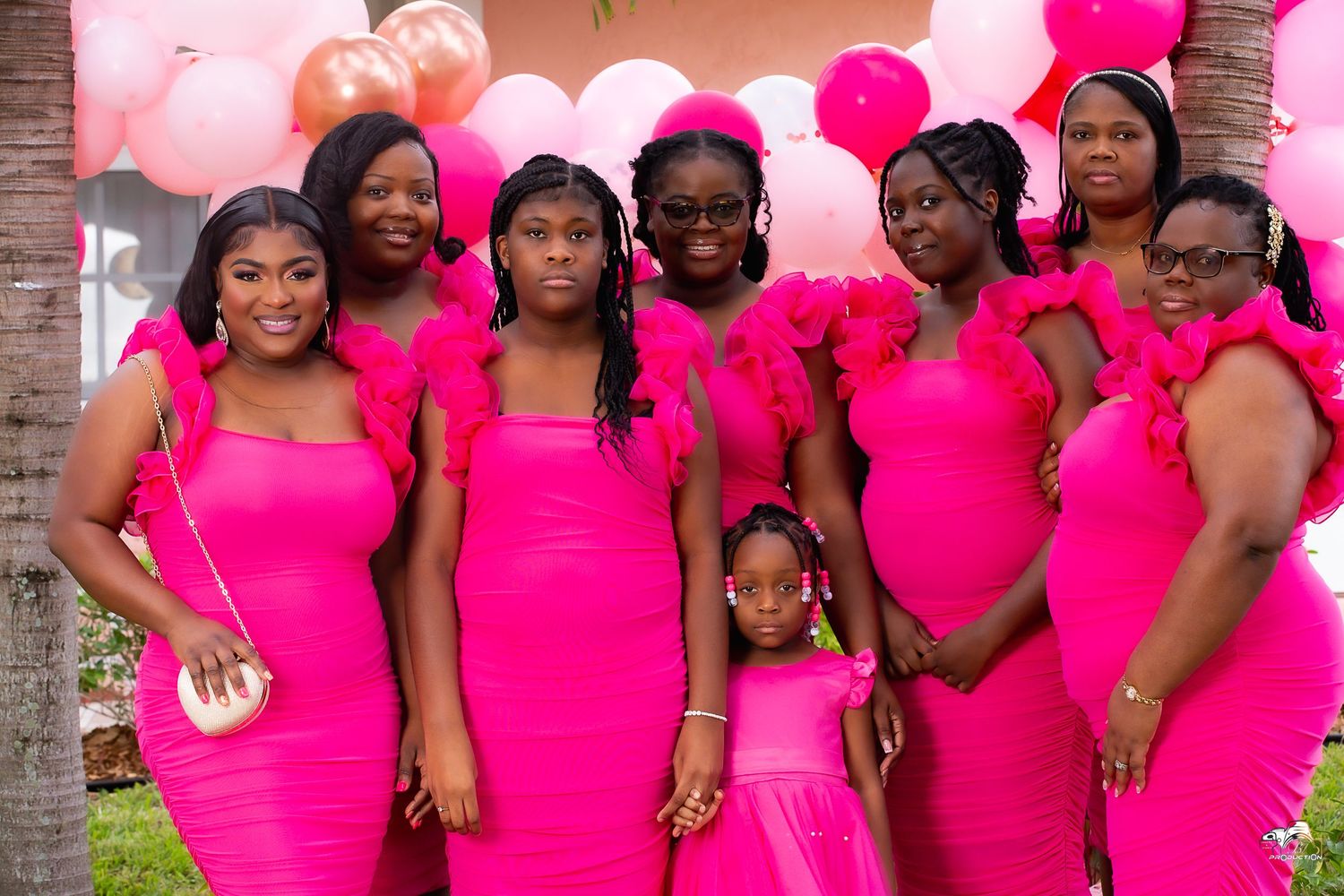 A group of attendees in matching bright pink dresses pose together at a formal celebration.
