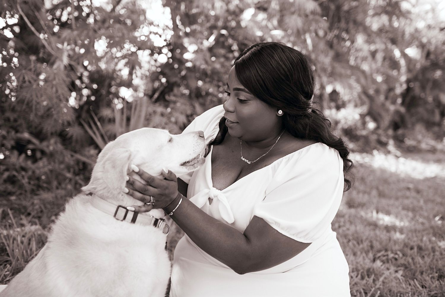 Black and white portrait of a person sharing a tender moment with their white dog outdoors.