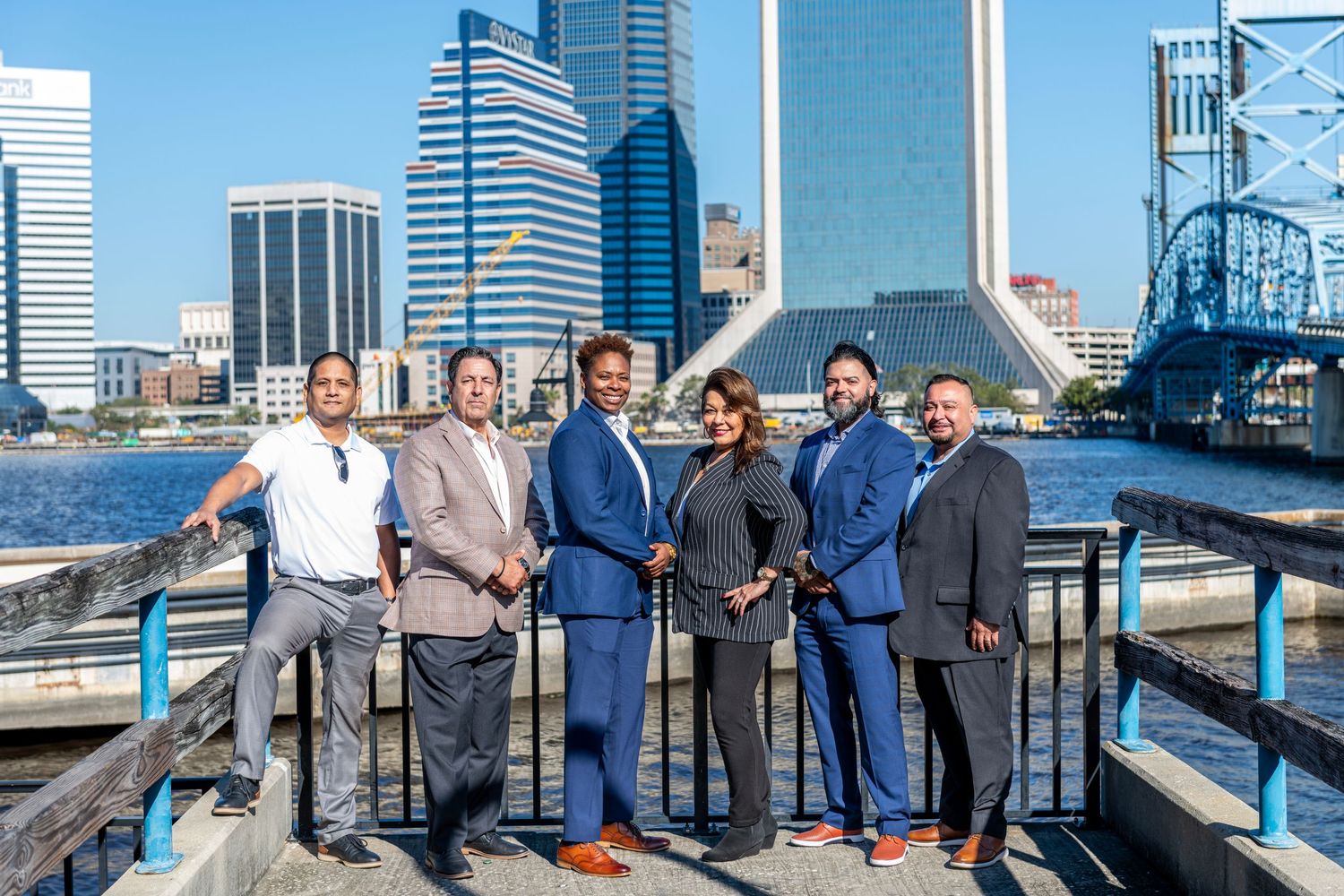 Business professionals gather on riverfront terrace with Jacksonville skyline and Main Street Bridge in background.