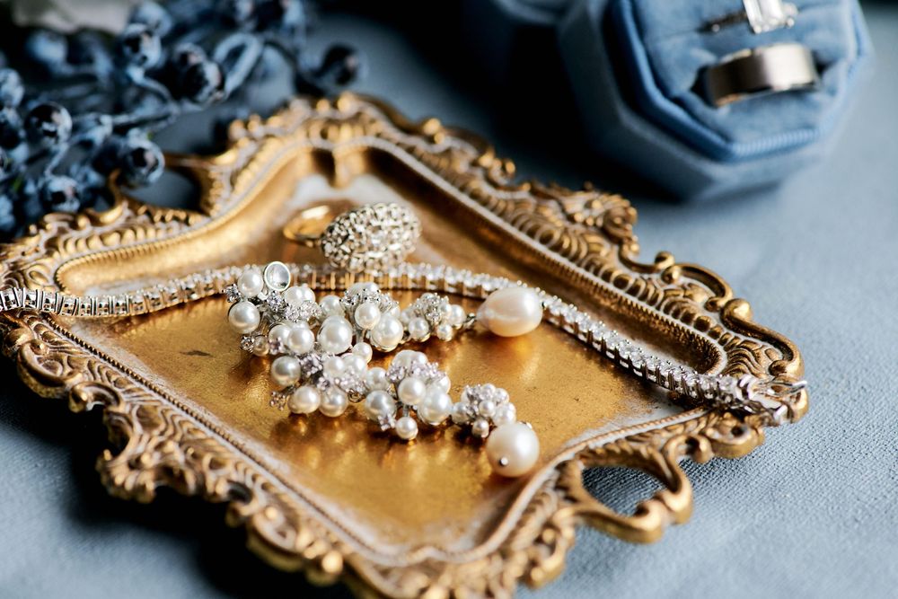 Elegant pearl and crystal bridal jewelry displayed on a vintage gold ornate tray with blue silk fabric.