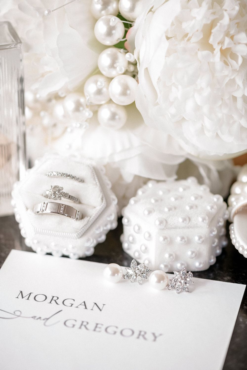 Elegant wedding details with white floral decorations, pearl accents, and name cards reading Morgan and Gregory.