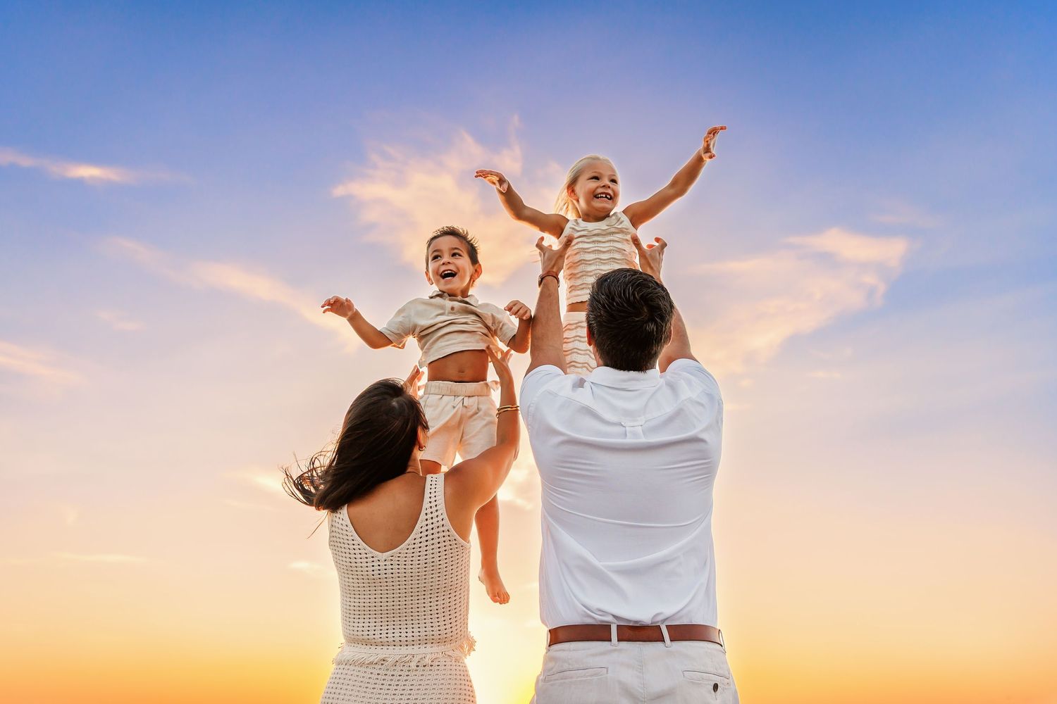 Mom and dad throw the laughing children into the colorful sunrise sky while they giggle and play together on the beach.