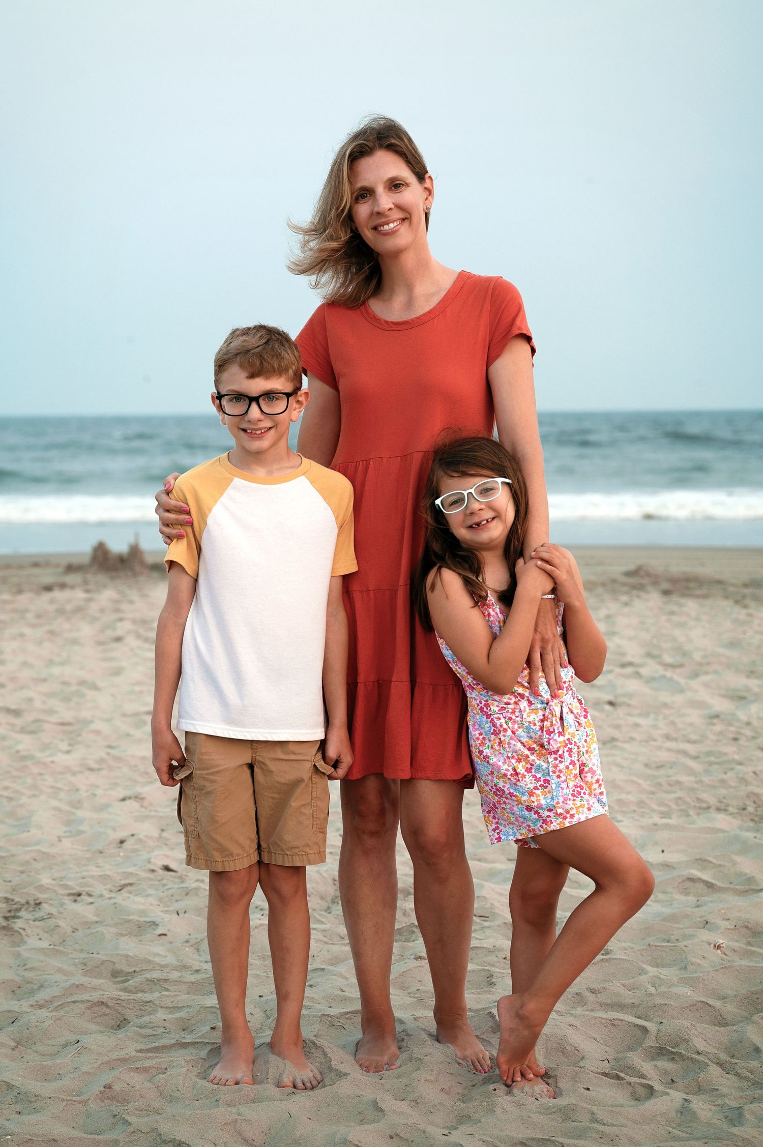 A family poses together on a sandy beach with the ocean in the background.