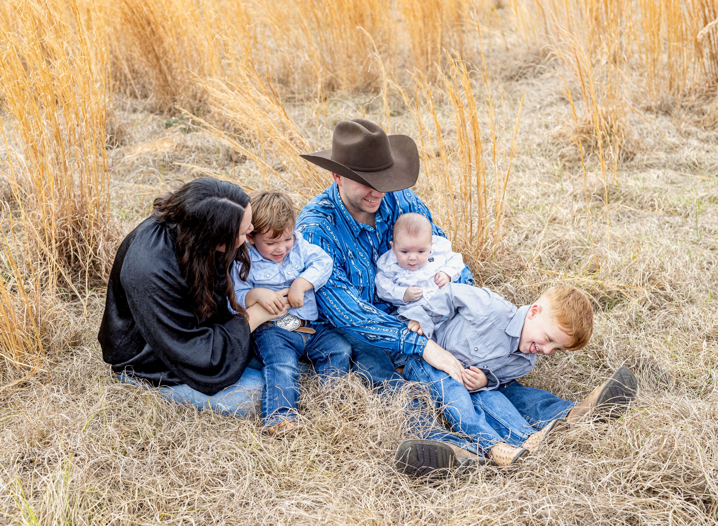 A family lies together in golden autumn grass during an outdoor photo session at sunset.