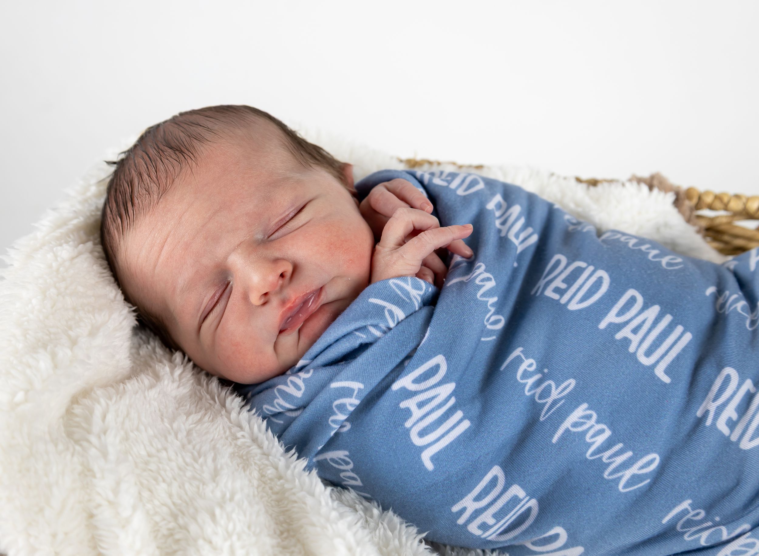 A sleeping newborn baby wrapped in a blue and white swaddle blanket rests on a soft white blanket.