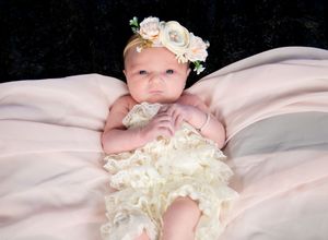 A baby wearing a white ruffled dress and floral headband lies on pink fabric in a series of connected photos.
