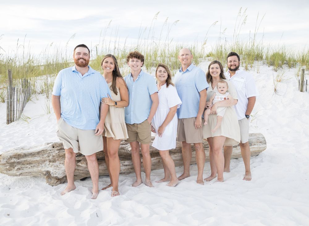A group poses together on a pristine white sand beach wearing coordinated light blue and white outfits.
