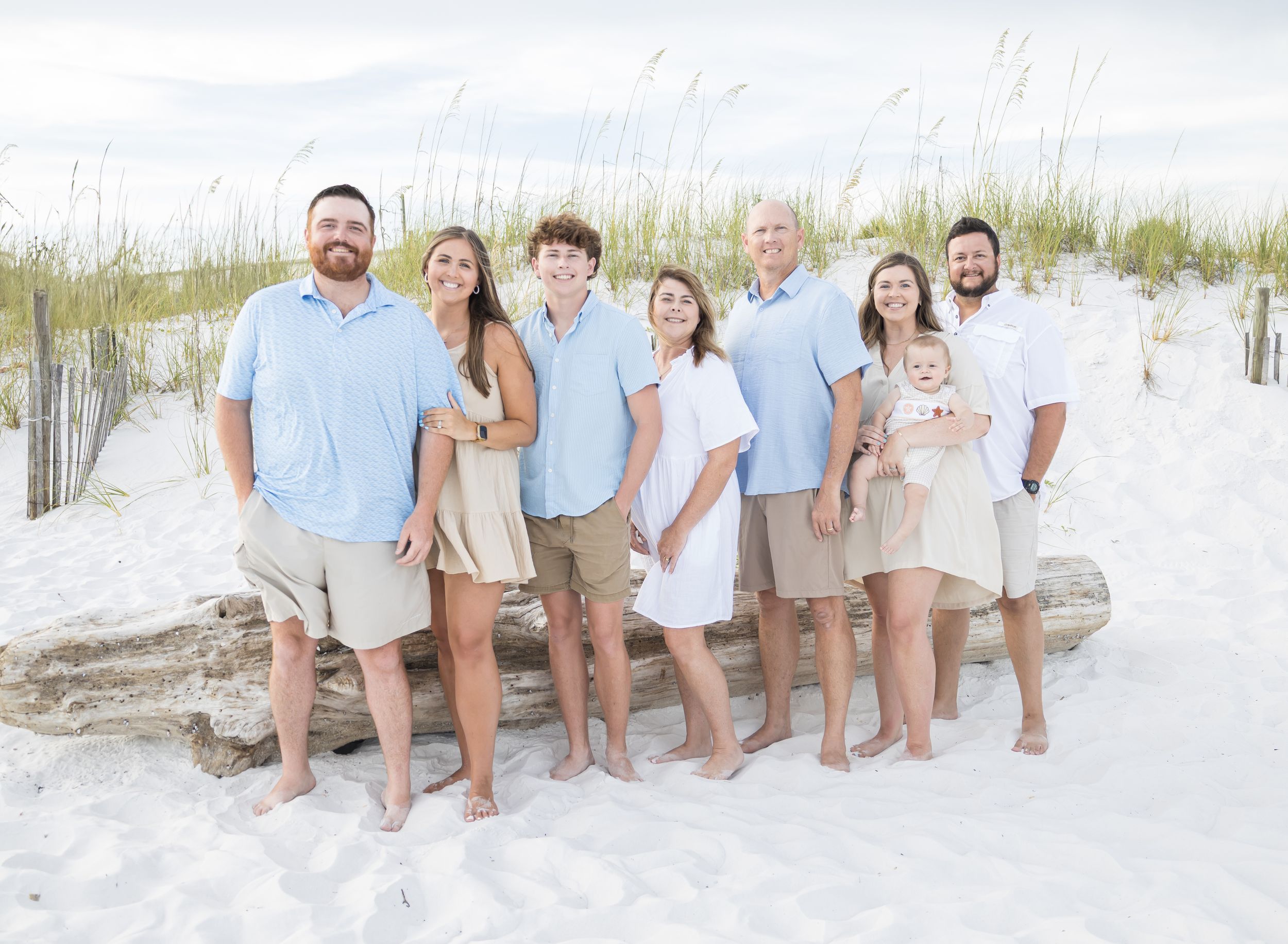 A group poses together on a pristine white sand beach wearing coordinated light blue and white outfits.