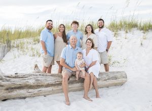 Family in white and blue outfits sitting together on a sandy white beach during sunset.