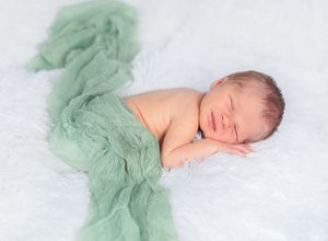 Sleeping newborn baby lying on soft mint green fabric in artistic panoramic photo series.